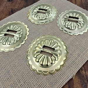 May include: Four circular gold-toned metal concho buckles featuring a scalloped edge and a central rectangular bar for strap attachment. Each piece displays a radial sunburst pattern with embossed ridges extending from the centre to the outer rim.