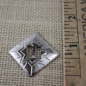 Pu&ograve; includere: Una fibbia in metallo argentato con un design a stella e un'apertura rettangolare. La fibbia misura circa 2,5 cm.