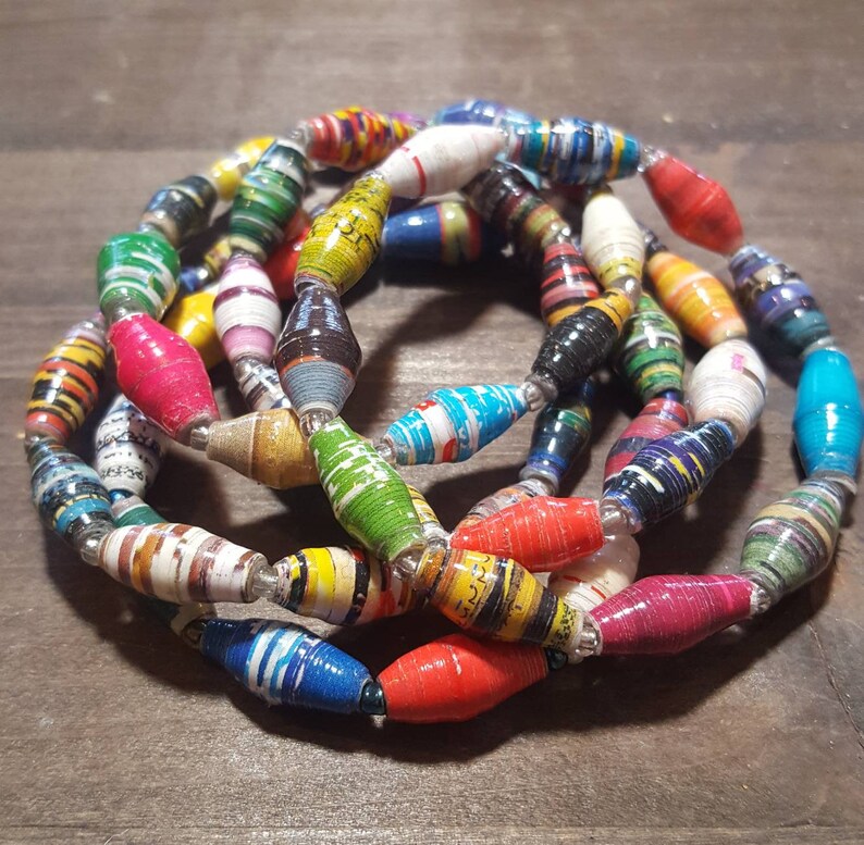 Op de afbeelding: Een kleurrijke ketting gemaakt van gerolde papier kralen. De kralen zijn in verschillende kleuren, waaronder rood, geel, blauw, groen en zwart. De ketting is gelaagd en lijkt handgemaakt te zijn.
