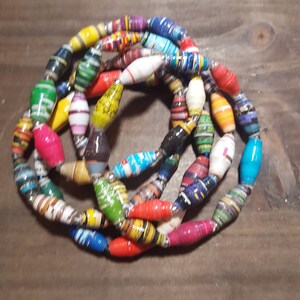 Op de afbeelding: Een kleurrijke ketting gemaakt van gerolde papier kralen. De kralen zijn in verschillende kleuren en patronen, waaronder rood, blauw, groen, geel en wit.
