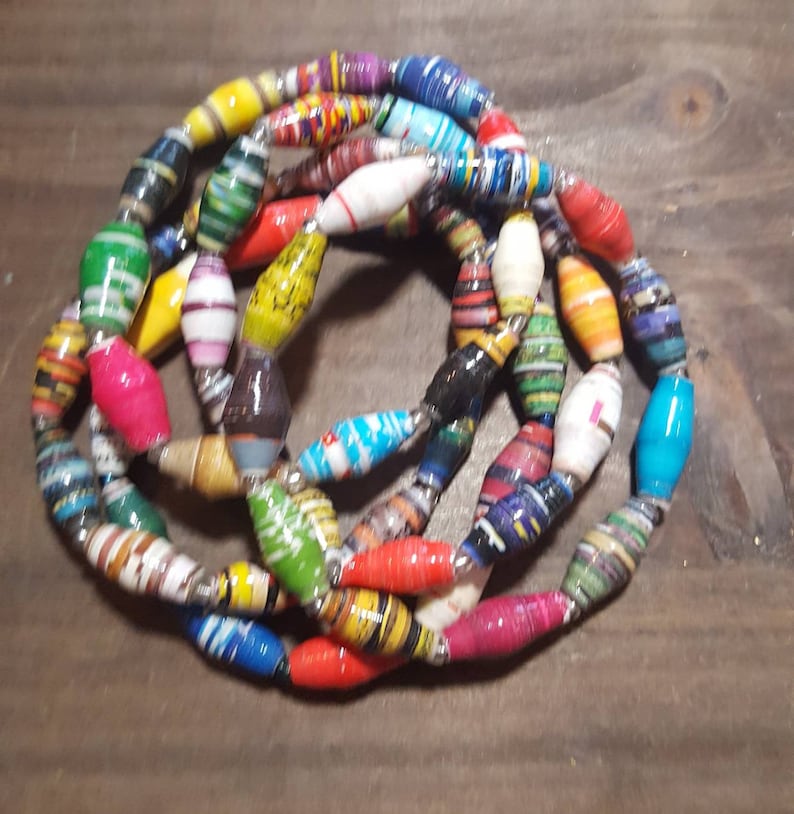 Op de afbeelding: Een kleurrijke ketting gemaakt van gerolde papier kralen. De kralen zijn in verschillende kleuren en patronen, waaronder rood, blauw, groen, geel en wit.