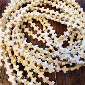 May include: A strand of white howlite beads in the shape of crosses. The beads are strung on clear elastic cord.