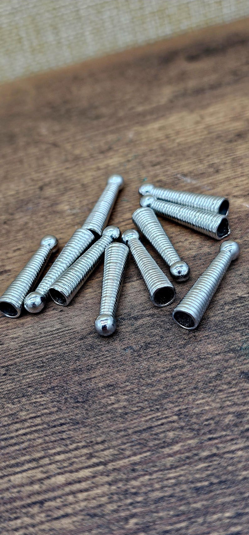 Op de afbeelding: Close-up van verschillende kleine, zilverkleurige metalen voorwerpen. Elk voorwerp heeft een afgeronde kop en een spiraalvormig lichaam. De voorwerpen liggen verspreid op een houten oppervlak.