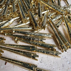 May include: A pile of gold-colored metal tips with a floral design. The tips are pointed and have a hole at the top.