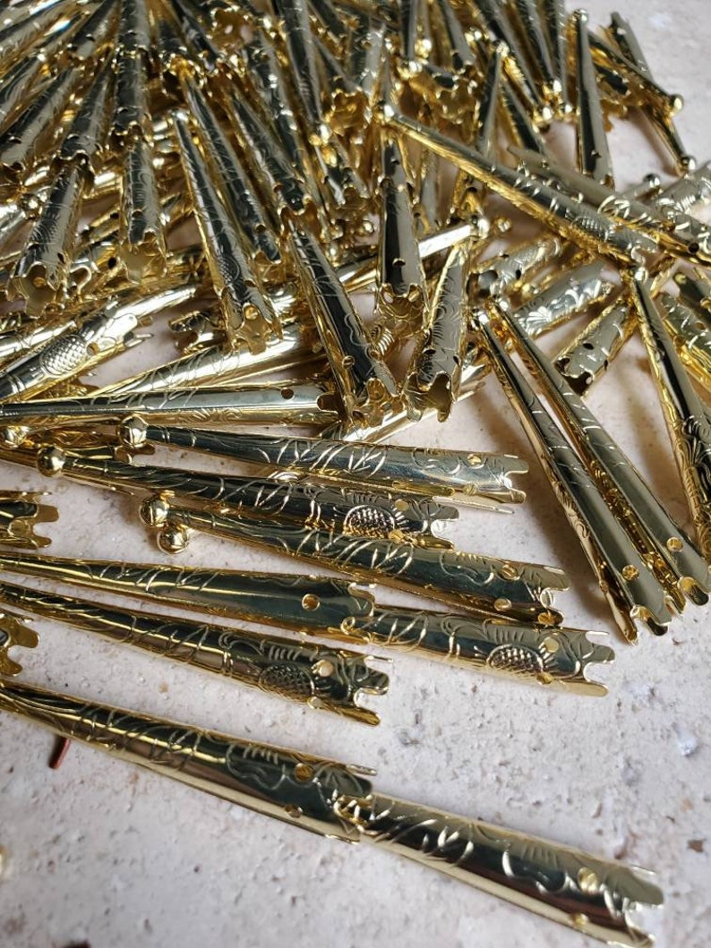 May include: A pile of gold-colored metal tips with a floral design. The tips are pointed and have a hole at the top.