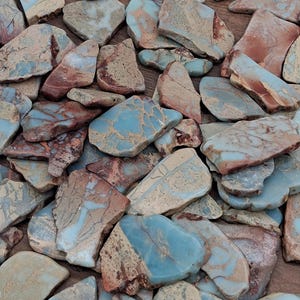 May include: A collection of irregularly shaped stones with a mix of colors, including blue, brown, and beige. The stones have a natural, textured appearance, with some displaying a marbled effect. The arrangement suggests a focus on natural materials and potential use in crafts or decor.