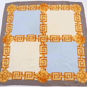 Könnte beinhalten: Ein grauer Seidenschal mit einem geometrischen Muster aus goldenen Ketten und Medaillons. Der Schal hat einen hellblauen und cremefarbenen Hintergrund.