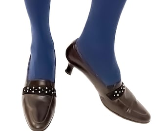 Puede incluir: Un par de zapatos de tacón de cuero marrón con una tira negra adornada con joyas sobre el empeine. Los zapatos se llevan con medias azules.