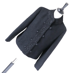 May include: A black wool jacket with a high collar and a decorative trim around the front. The jacket has a double-breasted closure with buttons.