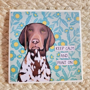 Può includere: Un Bracco tedesco a pelo corto marrone e bianco con uno sfondo floreale. Il cane sta guardando la fotocamera. Il testo "Keep Calm and Point On" è scritto in bianco su sfondo nero.