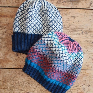 May include: Two knitted hats with geometric patterns. The top hat is white with a blue diamond pattern and a navy blue brim. The bottom hat is a multi-colored pattern with shades of blue, pink, and white.
