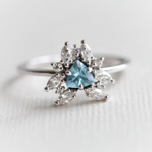 May include: A silver ring with a blue triangular gemstone surrounded by smaller clear gemstones.