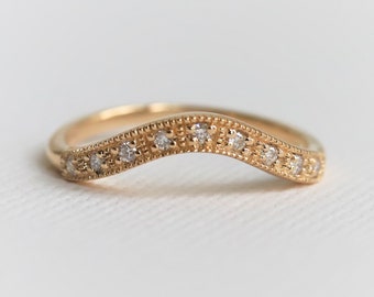 May include: A gold band with a curved shape and a row of small diamonds.