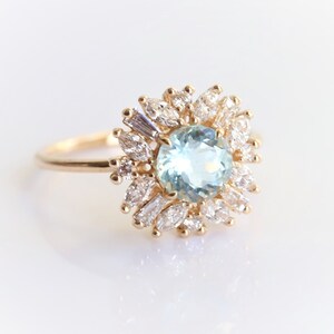 May include: A gold ring with a large, round, light blue aquamarine gemstone surrounded by smaller, clear diamonds in a flower-like design.