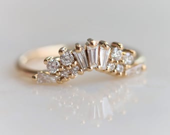 May include: A delicate gold band ring with a unique design featuring a cluster of small round and baguette-shaped diamonds set in a curved shape.