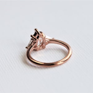 Puede incluir: Un anillo de compromiso de oro rosa con una piedra central grande de forma ovalada y dos piedras m&aacute;s peque&ntilde;as a cada lado. El anillo est&aacute; engastado en un dise&ntilde;o delicado e intrincado.
