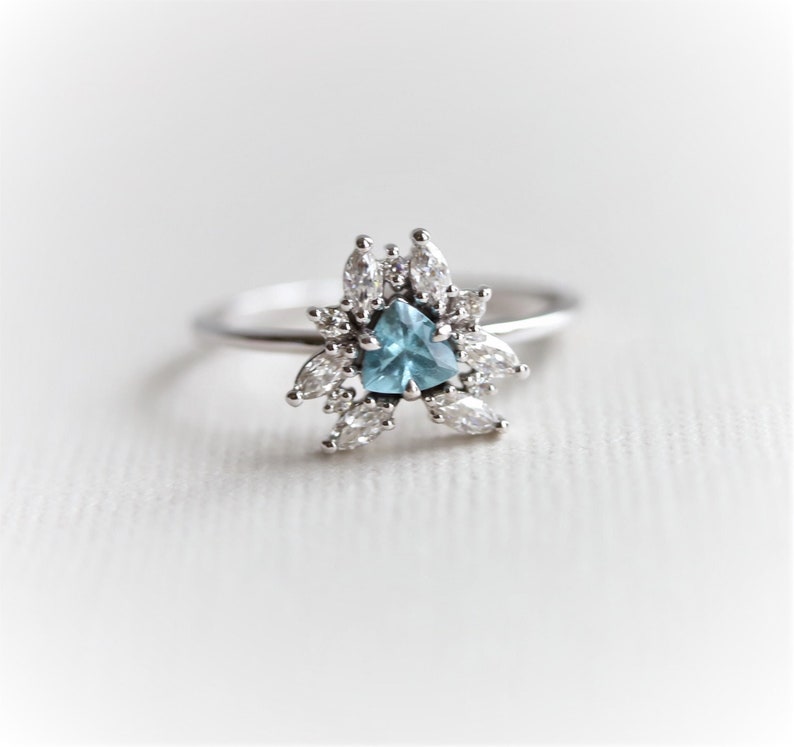 May include: A silver ring with a blue triangular gemstone surrounded by smaller clear gemstones.