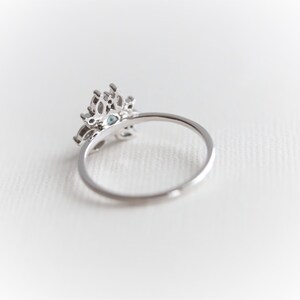 May include: A silver ring with a delicate, ornate design featuring a cluster of clear and blue gemstones. The ring is set on a white background.