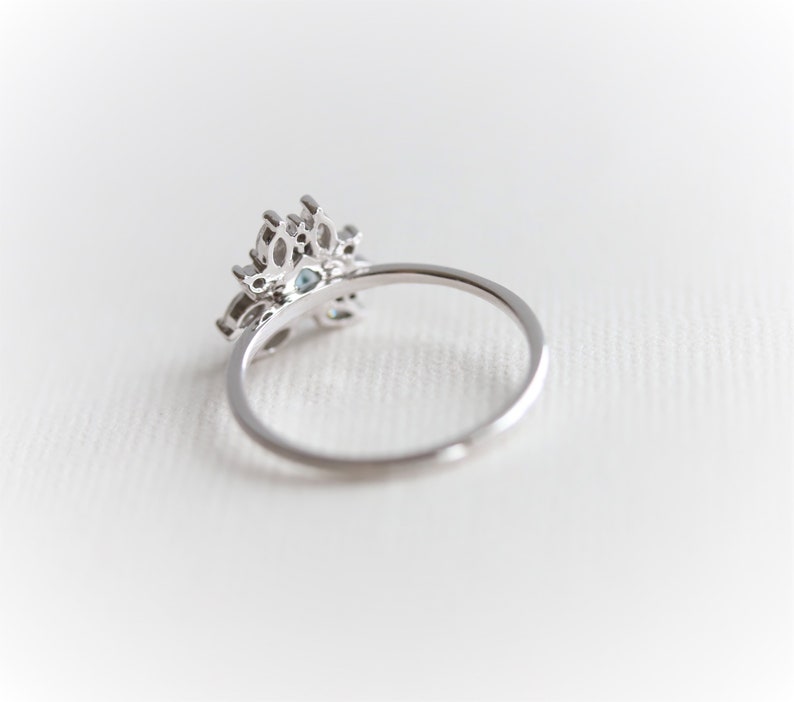May include: A silver ring with a delicate, ornate design featuring a cluster of clear and blue gemstones. The ring is set on a white background.