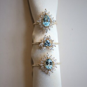 May include: Three gold rings with blue gemstones and diamond accents. The rings are displayed on a white fabric background.