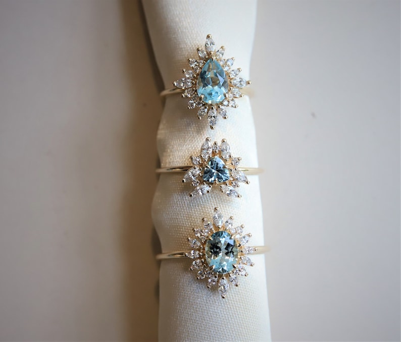May include: Three gold rings with blue gemstones and diamond accents. The rings are displayed on a white fabric background.