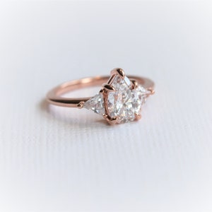 Puede incluir: Un anillo de compromiso de oro rosa con una piedra central en forma de pera y dos piedras de acento triangulares m&aacute;s peque&ntilde;as.