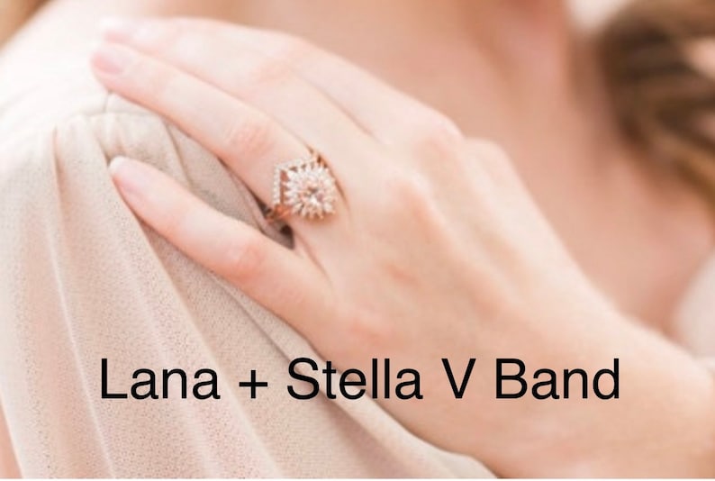 May include: A rose gold ring with a central, round, light-colored gemstone, surrounded by smaller stones in a starburst design. The ring is on a hand, with the text "Lana + Stella V Band" in the image.