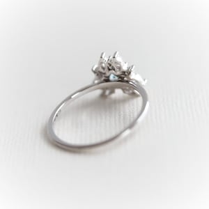 May include: A silver ring with a cluster of clear and blue gemstones. The ring is set on a white background.
