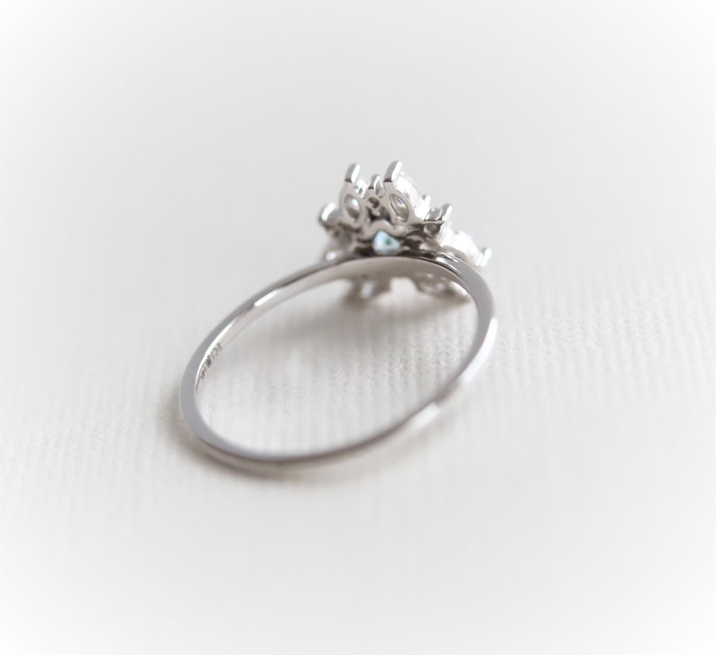 May include: A silver ring with a cluster of clear and blue gemstones. The ring is set on a white background.