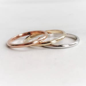 May include: Three simple, thin, gold-toned rings. The rings are stacked on top of each other. The top ring is silver, the middle ring is gold, and the bottom ring is rose gold.