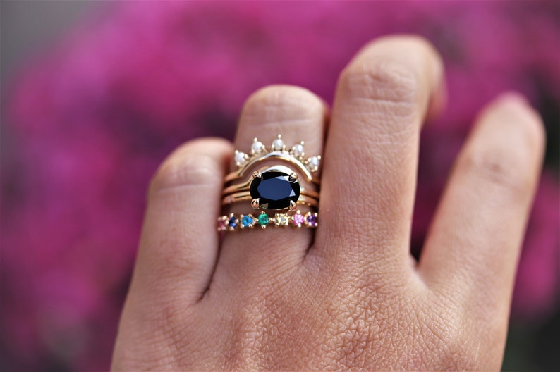 May include: A set of three gold rings with a black oval gemstone in the center ring. The top ring has a row of small white gemstones. The bottom ring has a row of colorful gemstones.