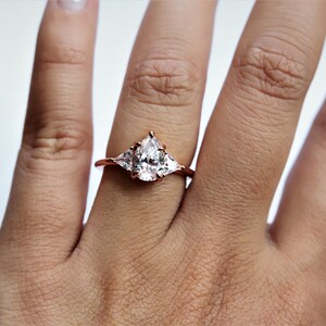 Puede incluir: Un anillo de oro rosa con una piedra central en forma de pera y dos piedras m&aacute;s peque&ntilde;as en forma de pera a cada lado.