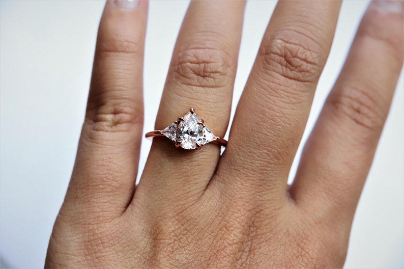 Puede incluir: Un anillo de oro rosa con una piedra central en forma de pera y dos piedras m&aacute;s peque&ntilde;as en forma de pera a cada lado.