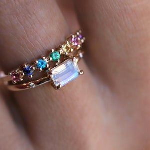 May include: A gold ring with a rainbow of small gemstones and a larger, rectangular moonstone.