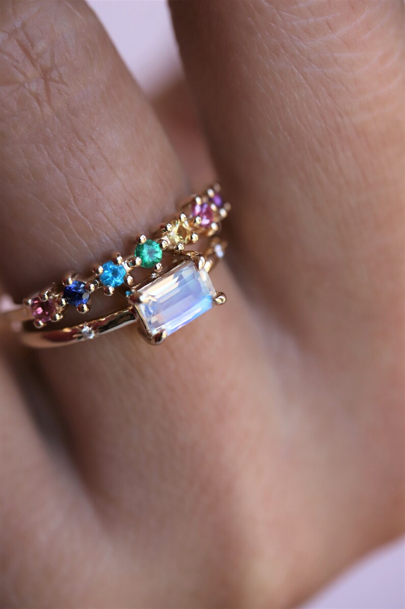 May include: A gold ring with a rainbow of small gemstones and a larger, rectangular moonstone.