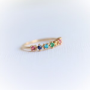 May include: A gold band ring with a row of colorful gemstones. The stones are pink, blue, turquoise, green, and orange.