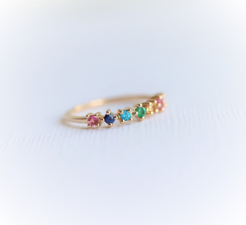 May include: A gold band ring with a row of colorful gemstones. The stones are pink, blue, turquoise, green, and orange.