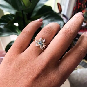 May include: A gold ring with a blue gemstone surrounded by smaller clear gemstones.