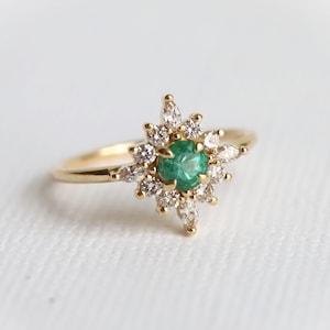 May include: A gold ring with a green emerald gemstone surrounded by smaller diamonds in a starburst design.