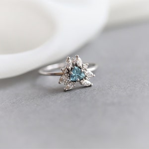 May include: A silver ring with a triangular blue gemstone surrounded by smaller clear gemstones.