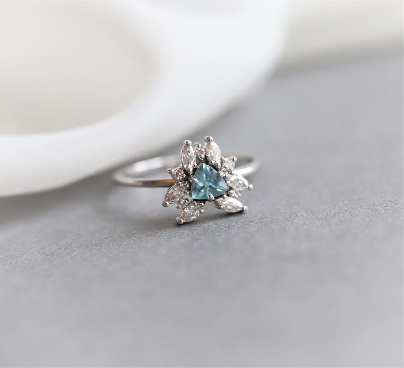 May include: A silver ring with a triangular blue gemstone surrounded by smaller clear gemstones.