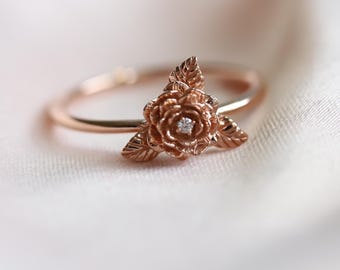 May include: A rose gold ring with a detailed rose design and a small diamond in the center.
