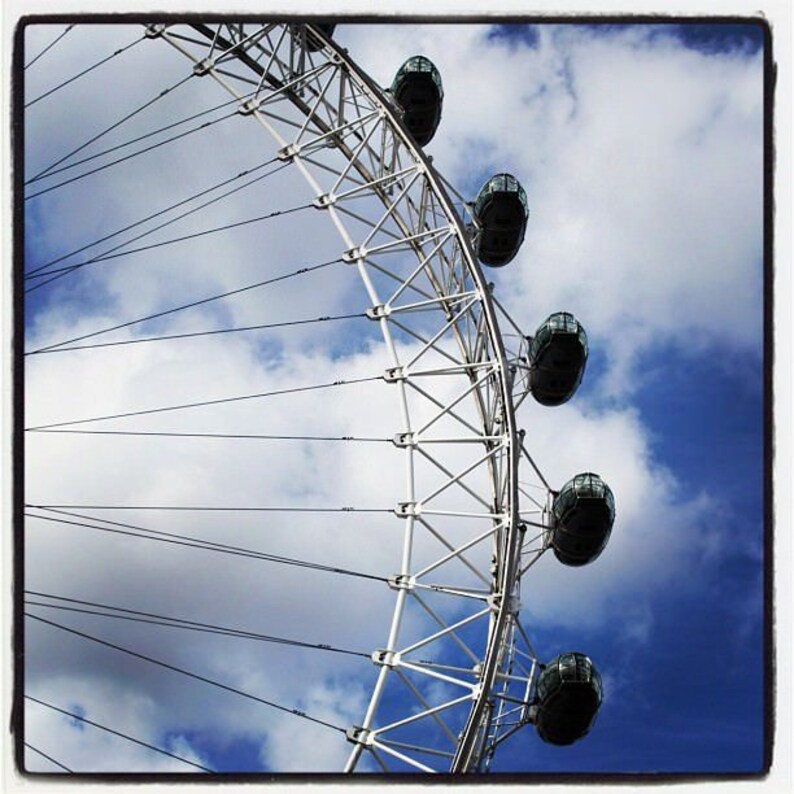 Puede incluir: Una noria blanca con g&oacute;ndolas negras contra un cielo azul con nubes blancas.