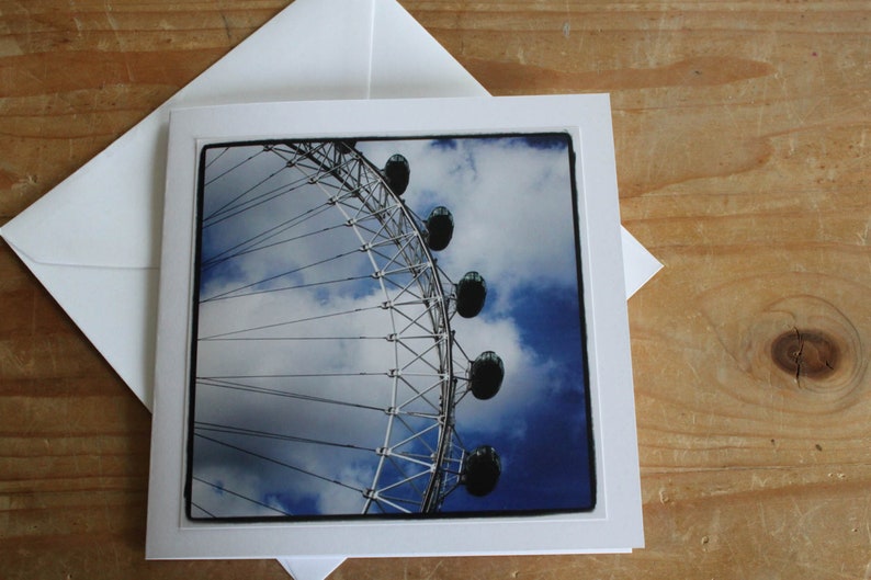 Puede incluir: Una vista cercana de la noria London Eye contra un cielo azul con nubes blancas. La rueda est&aacute; hecha de metal y tiene muchos radios. Las g&oacute;ndolas son visibles en la parte superior de la rueda.