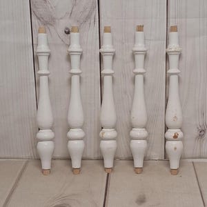 May include: Five white wooden table legs with a turned design. The legs are approximately 10 inches tall.