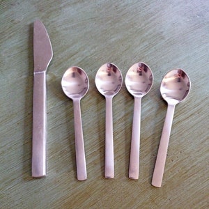 May include: A set of four silver spoons and a silver knife. The spoons are arranged in a row, with the knife to the left. The spoons are all the same size and shape, and they have a shiny, polished finish.