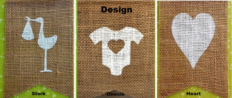 May include: Three burlap banners with white designs and green borders. The banners feature a stork carrying a baby, a onesie with a heart cutout, and a heart shape. The word "Design" is above the onesie.