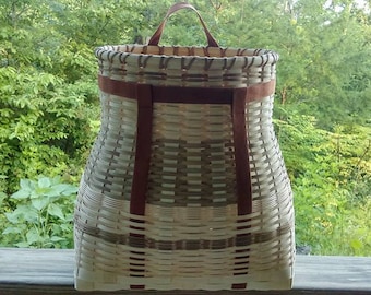 May include: A woven wicker backpack with brown leather straps. The backpack is made of natural materials and has a rustic look.