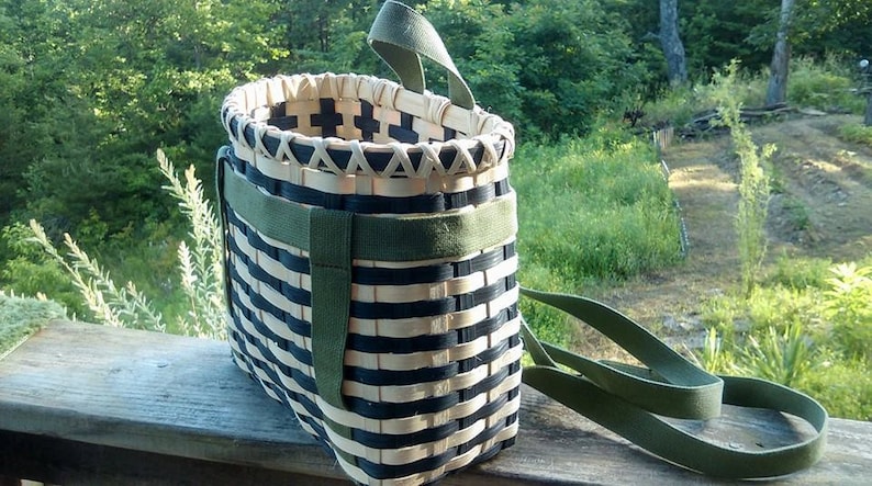 May include: A black and white woven basket with green straps. The basket is rectangular in shape and is made from natural materials. The straps are adjustable and can be used to carry the basket on the shoulder or as a backpack.