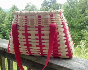 May include: A woven basket with red and white stripes and red handles. The basket is sitting on a wooden railing.